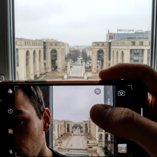 un selfie mal cadré du personnage avec une vue sur le quartier antigone de montpellier à partir de l'hotel Mercure. La photo doit être prise depuis le smartphone.