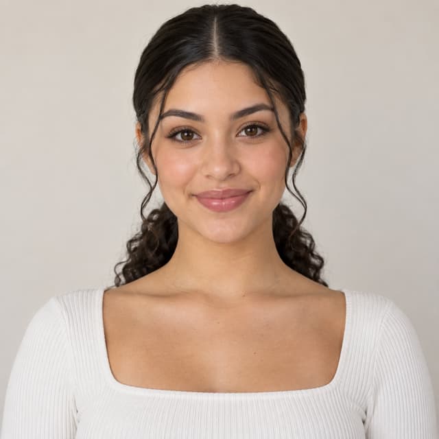 Girl with a thick, sleek low curly ponytail. All of her hair should be behind her body and her hair should be visible on both sides of her neck. This is a front view of the girl.