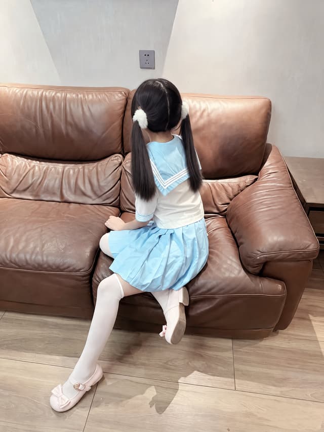 Edit the uploaded image. Keep the girl, her face, head shape, hair color, hairstyle, bangs, hair ties, clothing, sitting pose, hands, legs, shoes, brown leather sofa, table, wall, floor, lighting, shadows, camera angle, framing, and background completely unchanged.
Only modify her hair: the ponytail ends should reach approximately the level of her elbows, not lower. Keep the original twin-ponytail hairstyle and hair parting exactly the same. Make the extended hair look naturally connected to the existing hair, with realistic strands, natural volume, and consistent thickness.
Make the hair smoother, softer, silkier, and more well-groomed, with subtle natural shine and fine individual hair strands. Keep the original dark brown/black hair color and lighting. The longer hair should follow gravity naturally and rest realistically against her body.
Do not change anything else in the image. Do not alter her face, body proportions, clothing, pose, background, sofa, composition, camera perspective, or lighting. No beautification, no body reshaping, no face changes, no outfit changes, no background changes. The final result should look like the original photograph, with only the ponytails made longer and smoother.
