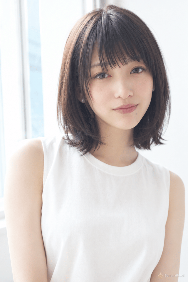 二十二歳の日本の女性。身長百五十八センチ、細くて小がら。黒い髪、肩につくかつかないかの長さのボブ、まゆにかかる前髪。肌は白い。うすい化粧、くちびるはうすい色。口をとじたまま口のはしだけを上げた、しずかな笑み。すこし首をかしげて、下からこちらを見ている。口の右下に小さなほくろ。耳に小さなパールのピアス。白いノースリーブのブラウス。清楚で、おちついていて、年より大人びて見える。窓からのやわらかい自然光、白い部屋、上半身。