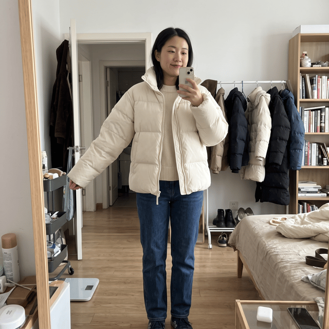 生成真实电商买家秀照片，一位20-40女性真实试穿奶油泡芙·空气感轻暖羽绒服，展示购买后的实际穿搭效果。女生身材自然，气质符合年轻有品位的女生，突出服装的【核心卖点：显瘦、修身、垂感、柔软、版型、设计细节】。
场景为真实消费者生活环境：【卧室穿衣镜前/咖啡店/商场/街头/办公室/旅行场景】，采用手机随手拍摄视角，不要商业棚拍感。
画面重点展示：
- 整体上身效果
- 衣服版型和身材修饰效果
- 面料质感和细节
- 日常搭配效果
- 真实购买后的满意状态
照片风格类似淘宝五星买家秀、小红书真实穿搭分享，高清手机摄影，自然光线，轻微生活滤镜，真实用户拍摄感，高还原度。
